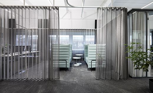 Zu sehen ist ein Büro, das mit dem Alu Net Vorhang von Création Baumann akustisch und optisch abgetrennt wurde.