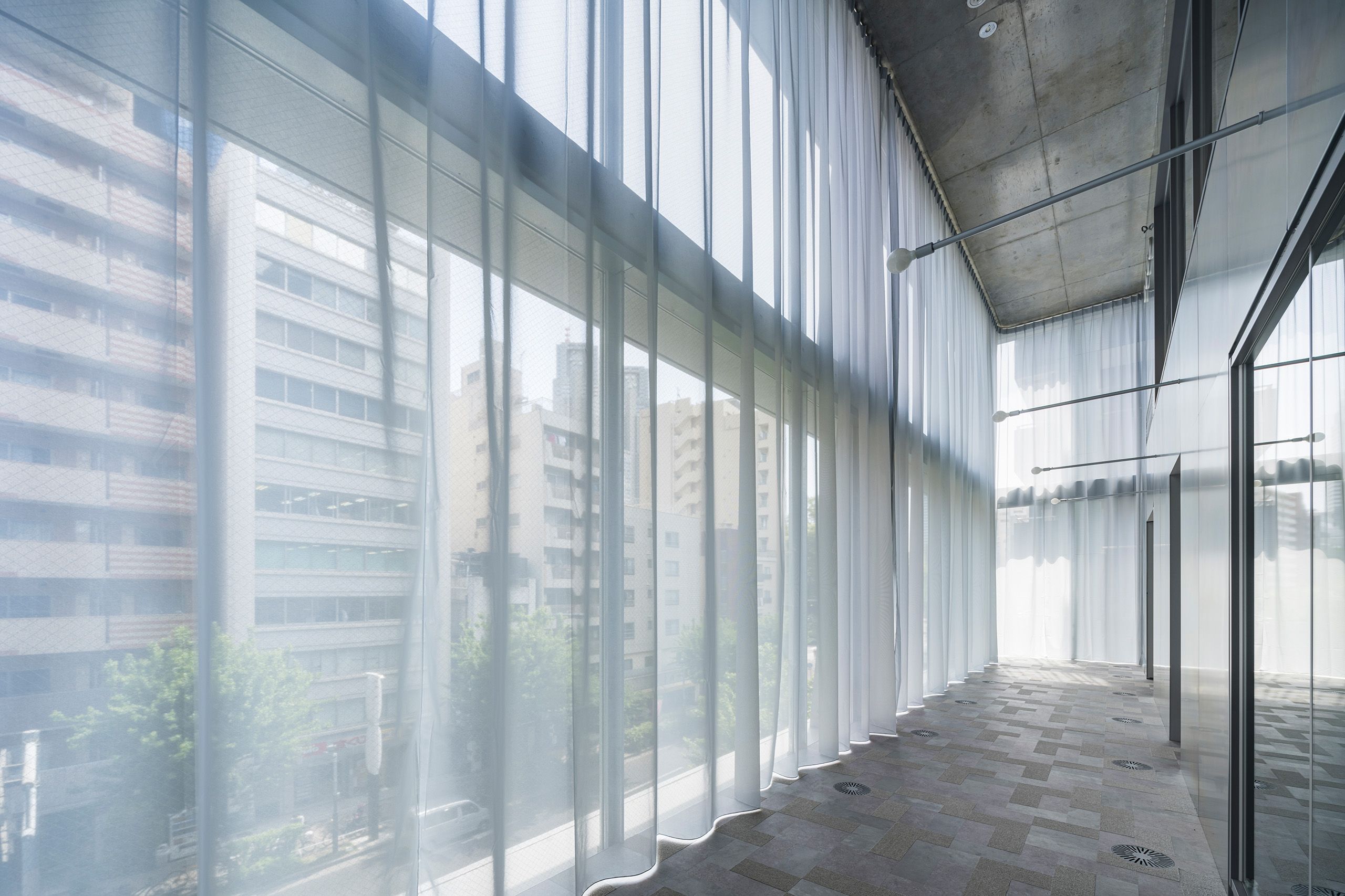 Offene Fensterfront mit Création Baumann Vorhang SHADOW. Blick auf Tokyo.