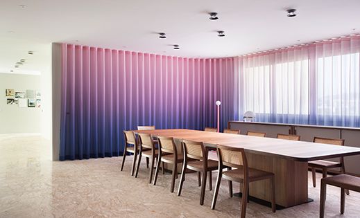 Zu sehen ist ein grosser Tisch mit lila SINFONIA CS Vorhängen von Création Baumann.