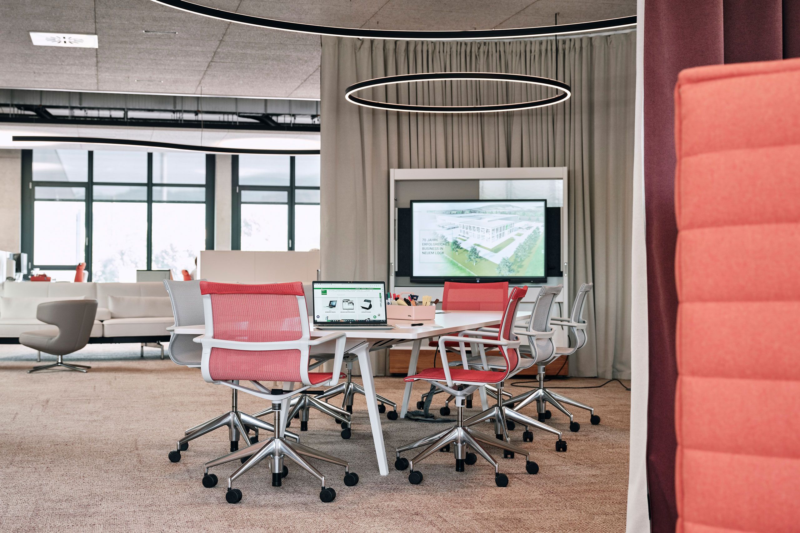 Offene Bürosituation mit Sitzungstisch und Präsentations-TV zoniert durch einen Akustiktrennvorhang.