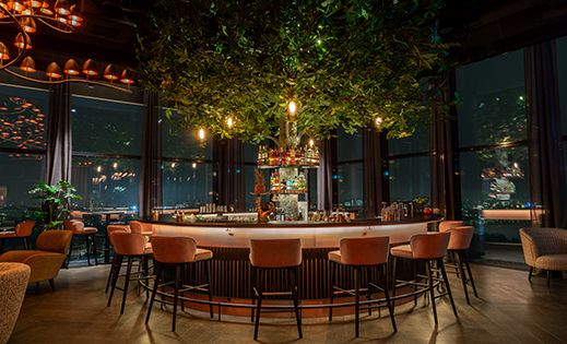 Im Zentrum des Bildes befindet sich eine stimmungsvoll beleuchtete Bar, die 3Sixty Bar - Stockholm, vor einer Panoramafensterfront.