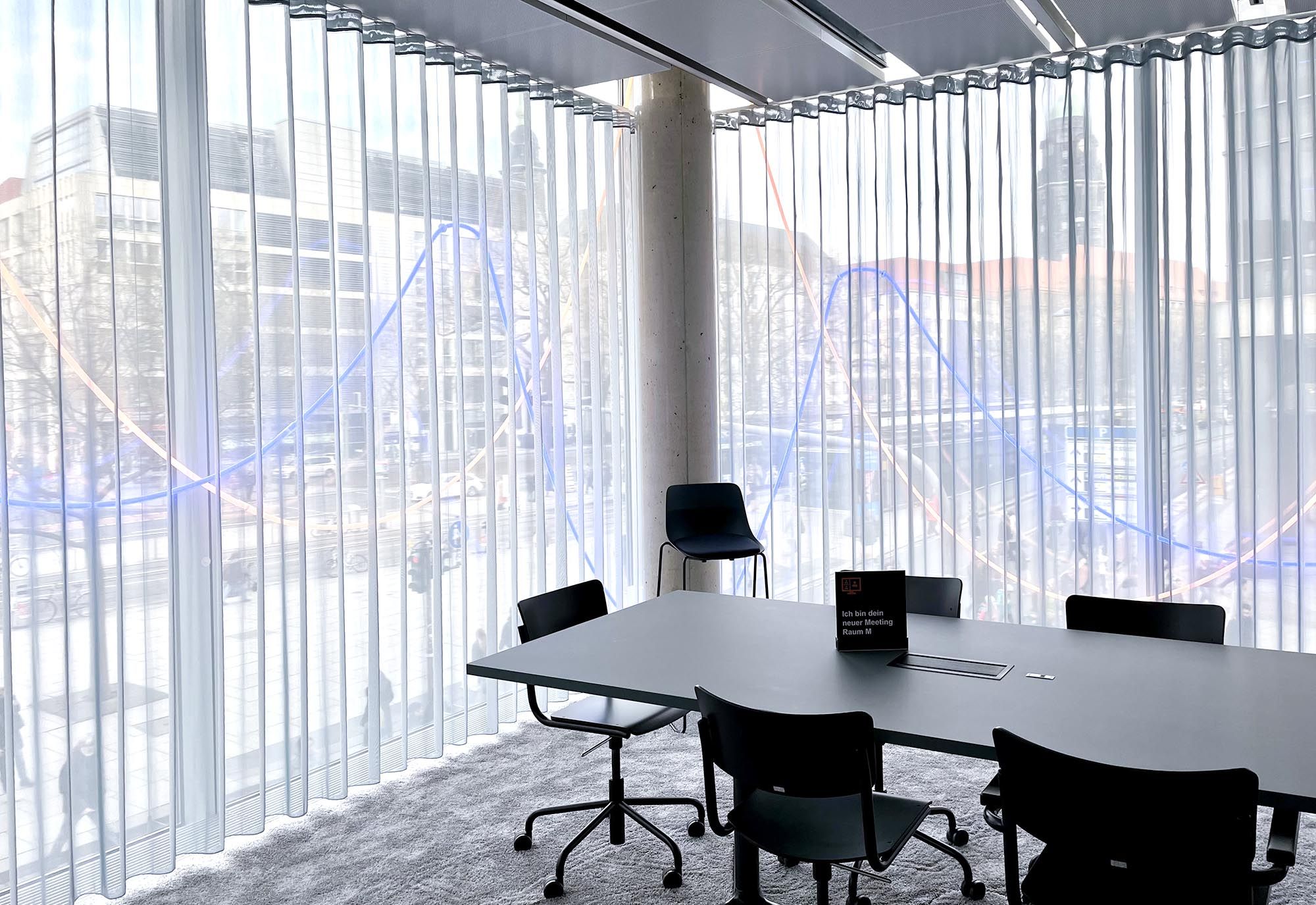 Transparenter Hitzeschutzvorhang FACE vor bodenhohen Fenstern in einem Sitzungszimmer.