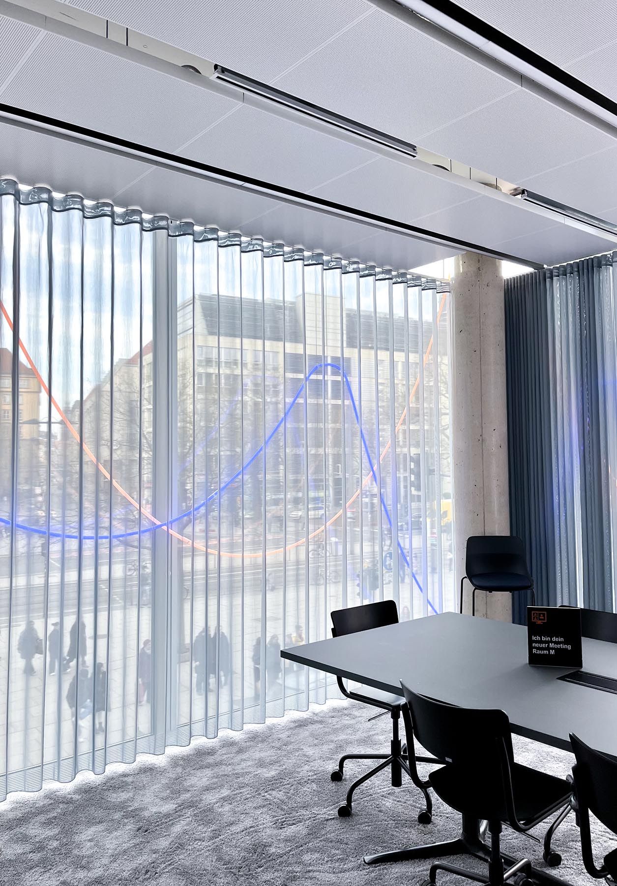 Transparenter Blendschutzvorhang FACE entlang einer Glasfront in einem Sitzungszimmer gezogen.